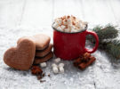 Cup of hot cocoa with marshmallows and Christmas gingerbread in the form of a heart on a snowy wooden background. Christmas card.