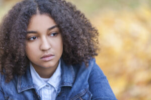 mixed race African American girl teenager female young woman outside in autumn or fall looking sad depressed or thoughtful
